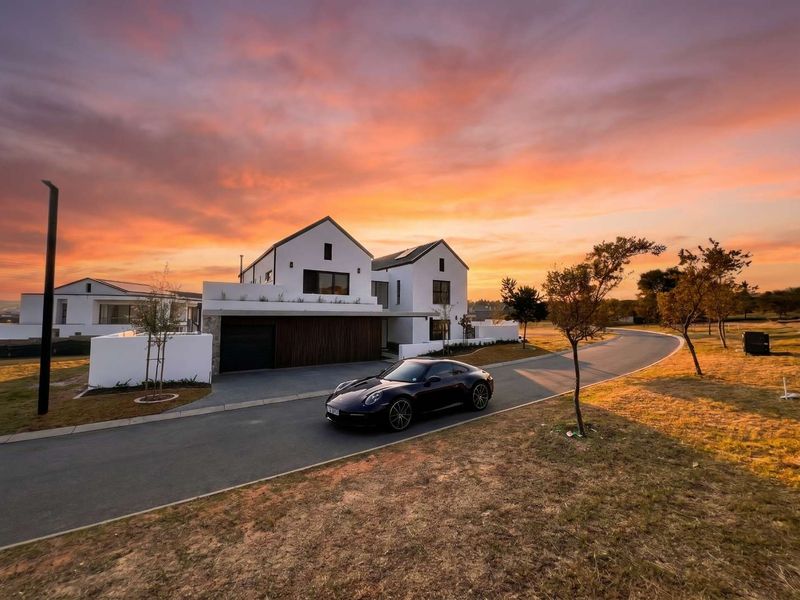 A modern architectural home featuring a clean white facade, pitched roof design, and paved driveway, captured during a vibrant sunset.