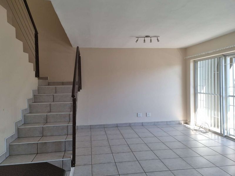 An open-plan living area featuring ceramic floor tiles, a staircase with a metal balustrade, and a sliding glass door with security bars.