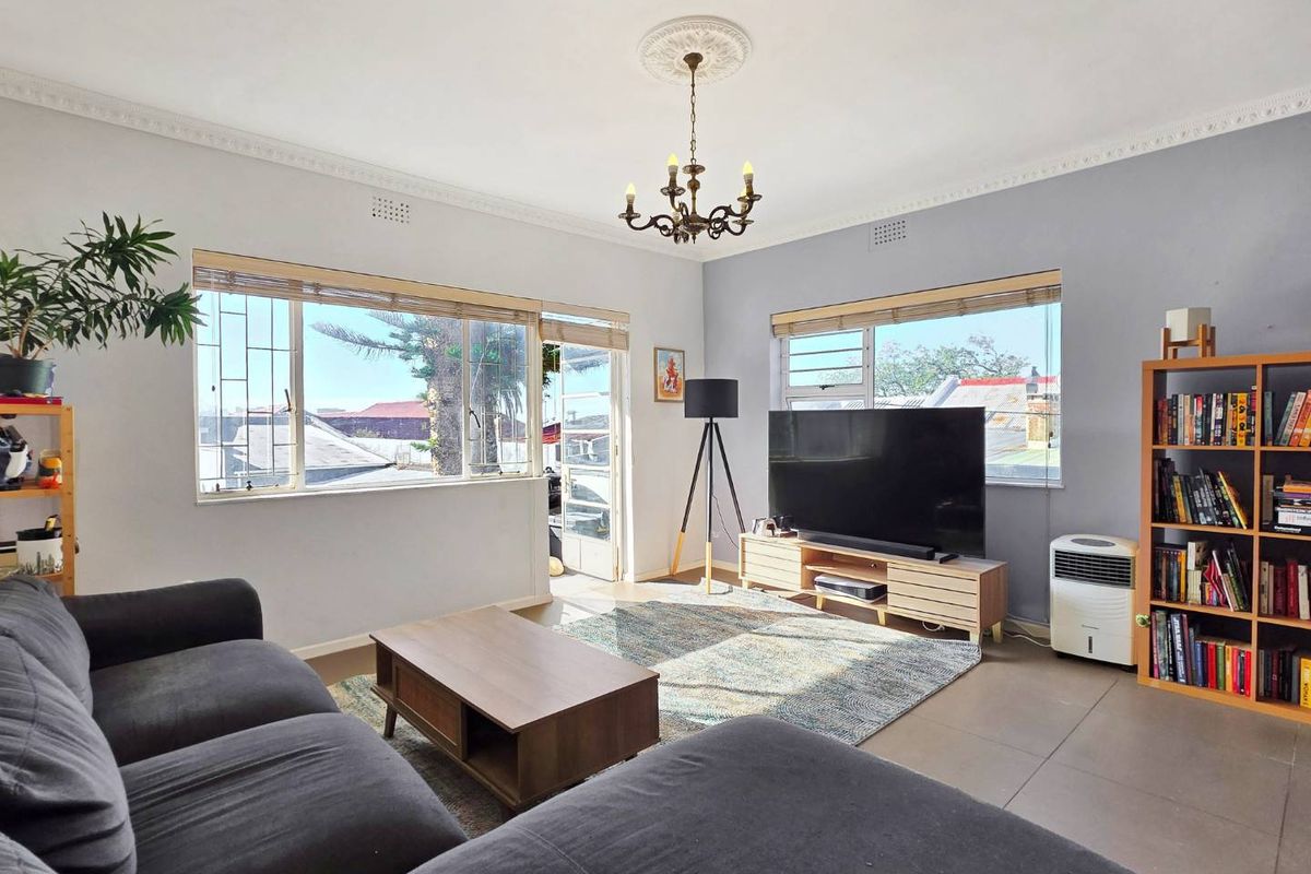 A bright living room featuring tiled floors, decorative ceiling cornice with a central rose, and large windows fitted with security bars.