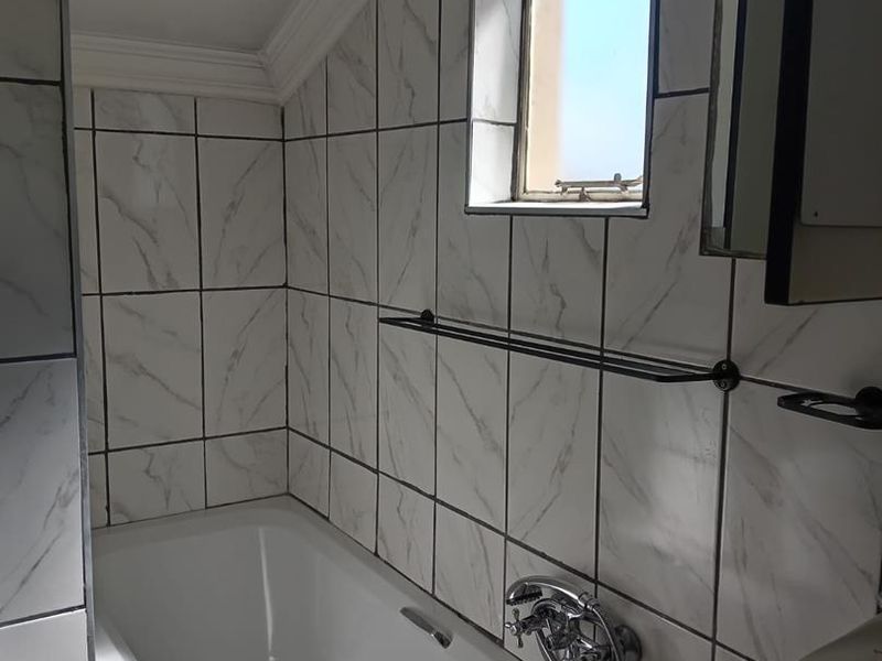 A bathroom featuring marble-look wall tiles, a built-in bathtub with chrome fixtures, and a small window under a sloped ceiling.
