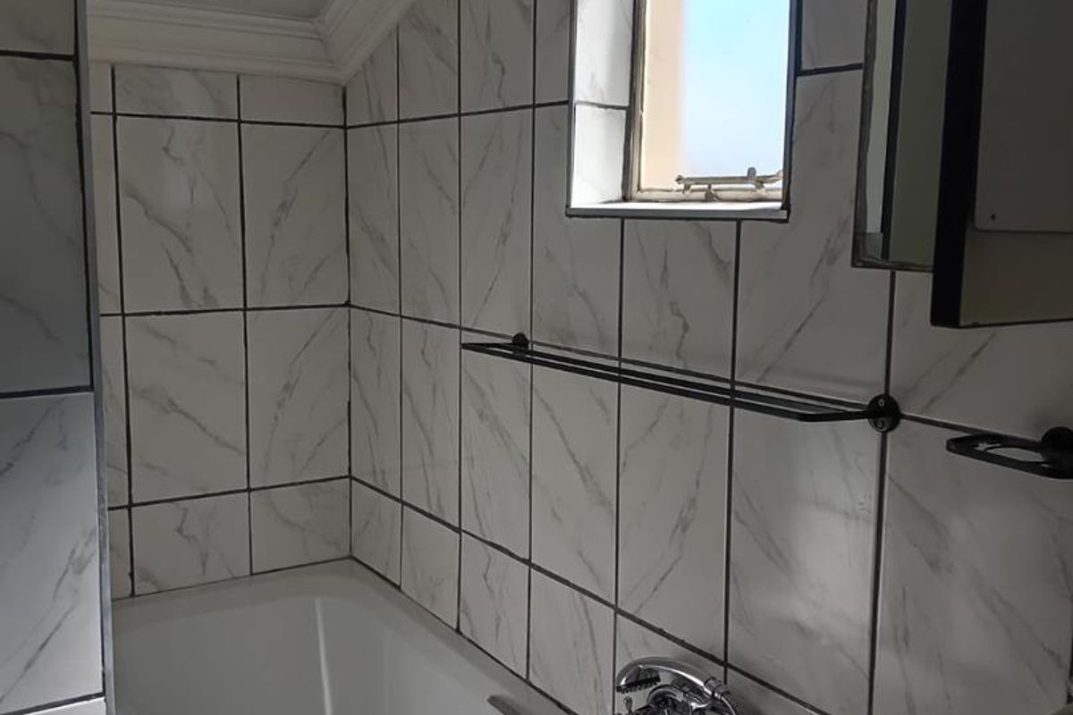 A bathroom featuring marble-look wall tiles, a built-in bathtub with chrome fixtures, and a small window under a sloped ceiling.