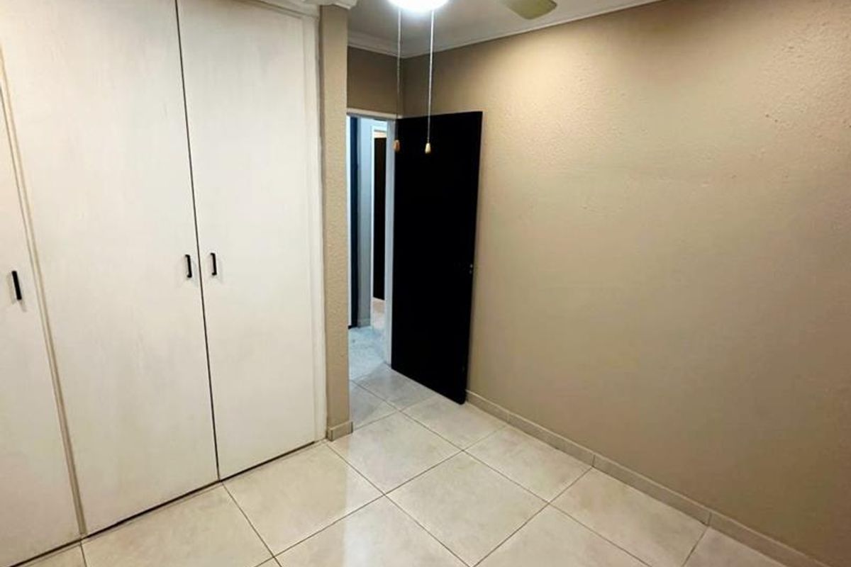 A clean, empty bedroom featuring neutral tiled flooring, built-in cupboards, and a central ceiling fan.