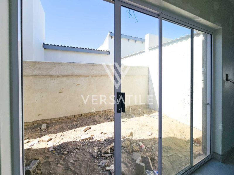 View of an unfinished rear courtyard area featuring a sliding glass door, boundary walls, and unlandscaped ground requiring completion.