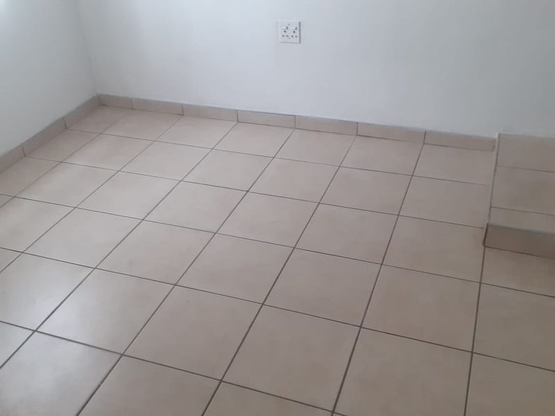 An empty room featuring neutral ceramic floor tiles, matching tiled skirting, and a clean white wall finish.
