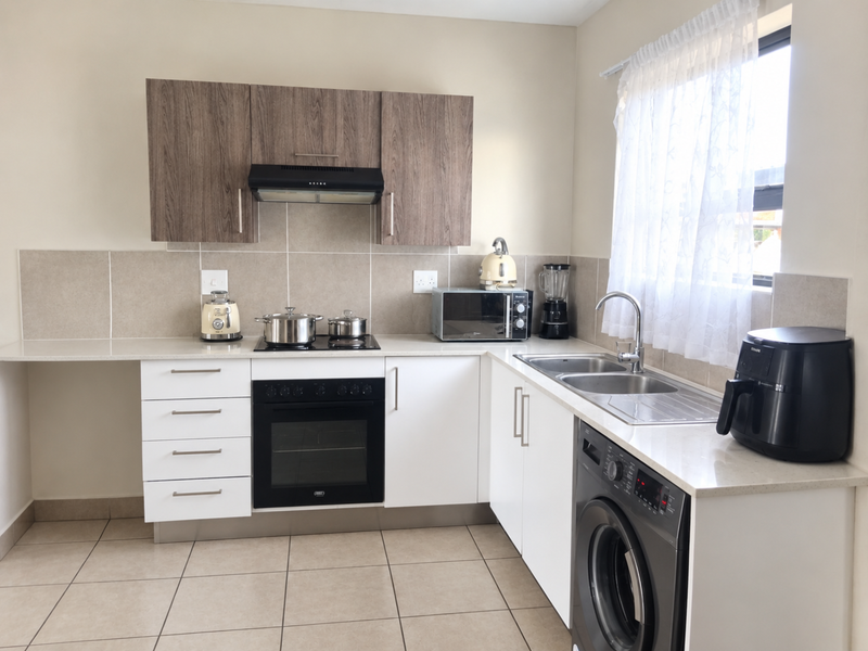 Modern kitchen featuring wood-grain upper cabinets, white lower cabinetry, stone countertops, tiled splashback, and integrated appliances including an oven and hob.