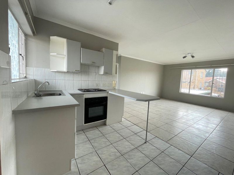 Open-plan kitchen and living area featuring tiled flooring, built-in cabinetry, integrated oven and hob, and a breakfast bar.