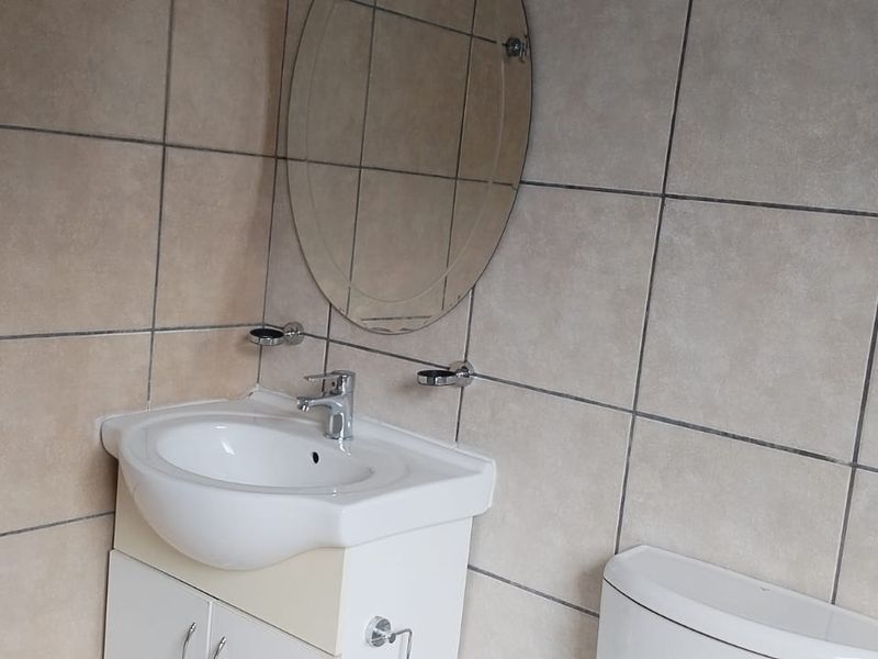 A functional bathroom featuring a vanity cabinet with a ceramic basin, chrome mixer tap, wall-mounted mirror, and full-height ceramic wall tiling.
