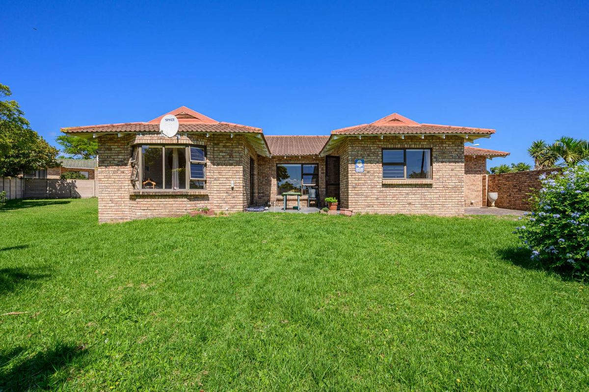 Rear view of a single-story brick house featuring a tiled roof, large windows, and a spacious lawn area.
