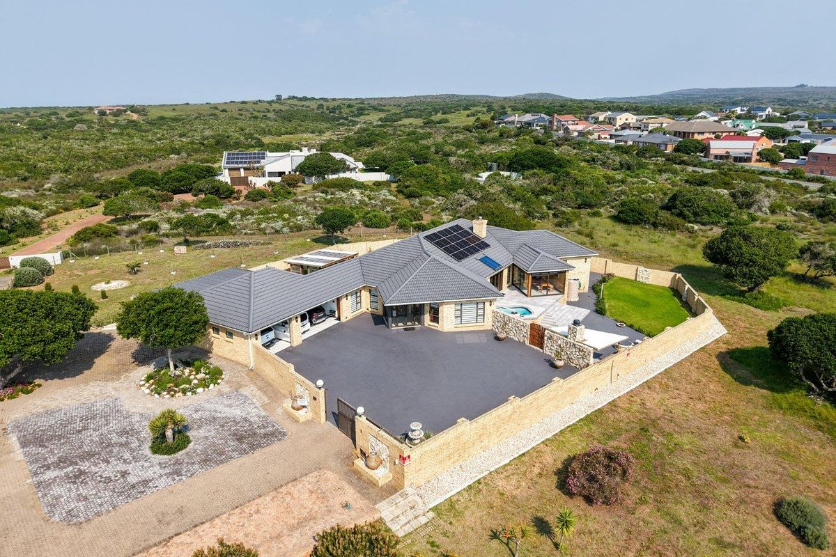 Aerial view of a modern residential property featuring a tiled roof with solar panels, a paved driveway, a swimming pool, and stone-clad boundary walls.