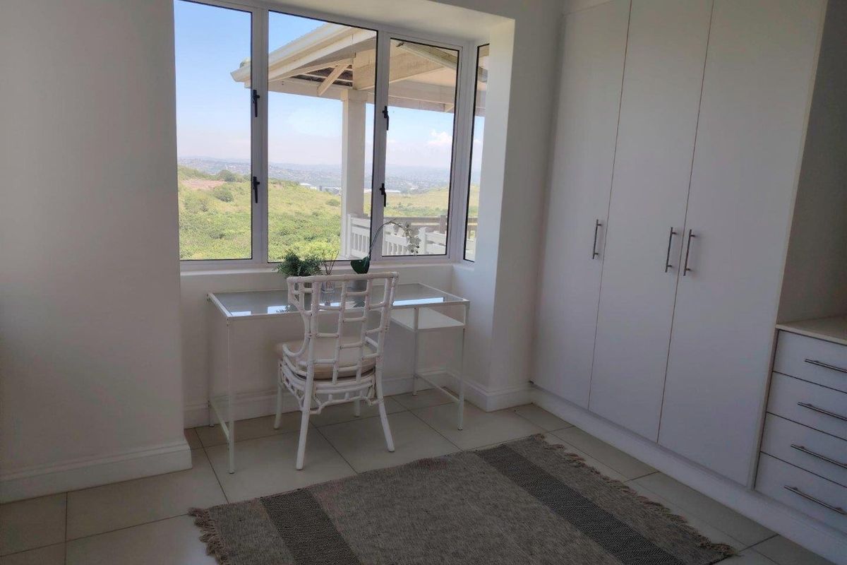 A bright bedroom featuring built-in cupboards, tiled flooring, and a large window offering scenic views.