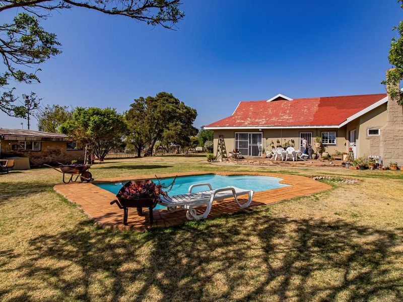 Spacious backyard featuring a swimming pool with brick surround, set against a large residence with a prominent stone chimney and red tiled roof.