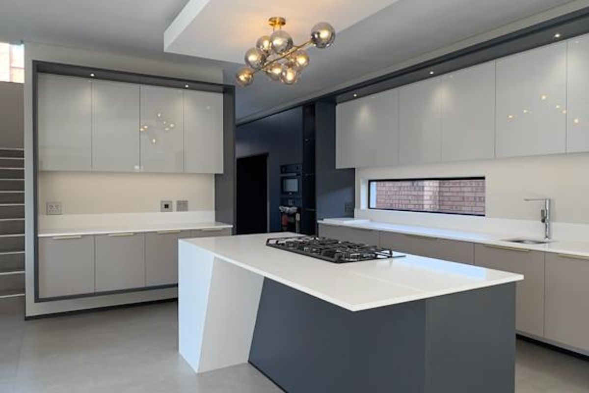 Modern, high-end kitchen featuring a central island with a gas hob, sleek handleless cabinetry, stone countertops, and integrated lighting.
