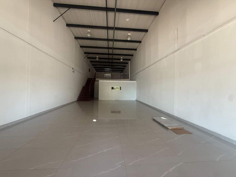 Spacious open-plan retail unit featuring high ceilings with exposed steel trusses, polished tiled flooring, and a mezzanine level accessed by a staircase.