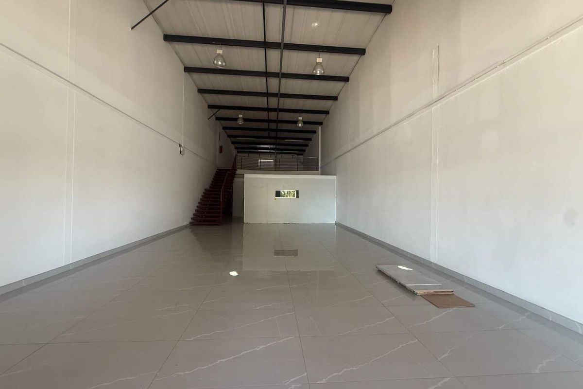 Spacious open-plan retail unit featuring high ceilings with exposed steel trusses, polished tiled flooring, and a mezzanine level accessed by a staircase.