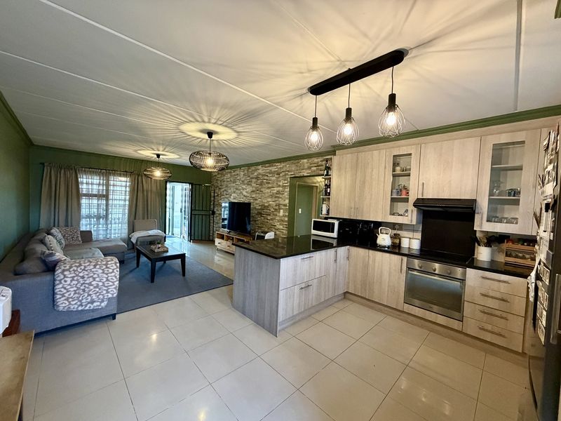 Spacious open-plan living area featuring a modern kitchen with granite countertops, built-in oven, and a stone feature wall, leading to an outdoor patio.