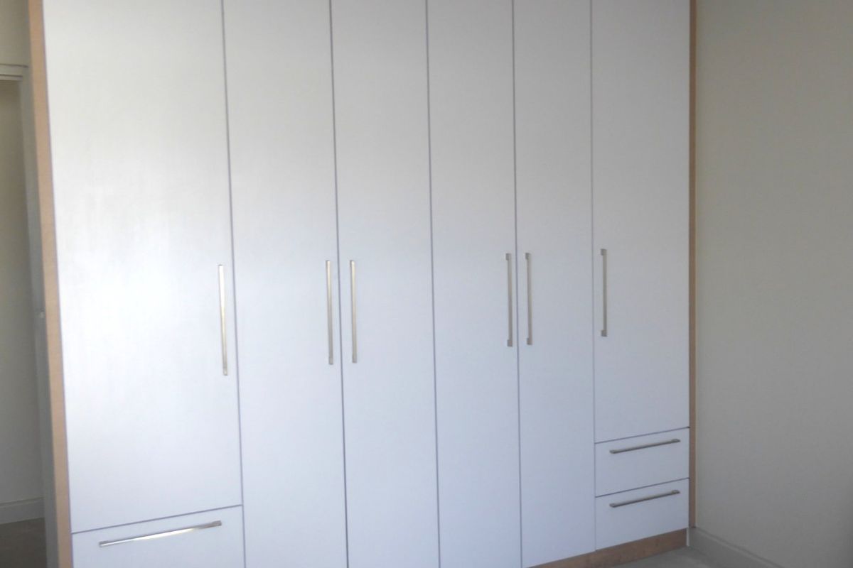 A bedroom featuring a large, modern built-in wardrobe with white cabinetry and integrated storage drawers.