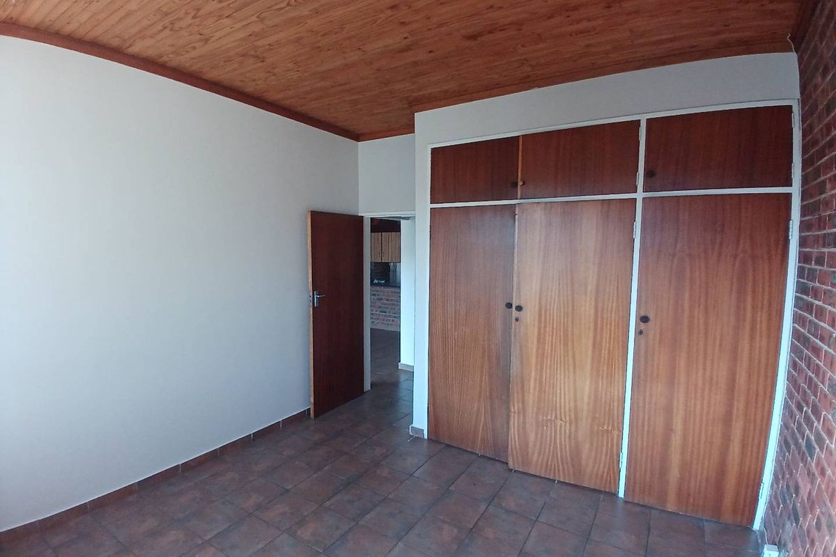 A bedroom featuring tiled flooring, a timber-clad ceiling, and built-in wooden cupboards, with an adjacent room visible through the doorway.