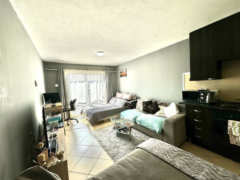 Open-plan living area featuring tiled flooring, a compact kitchen with dark cabinetry, and a sliding glass door providing access to the exterior.