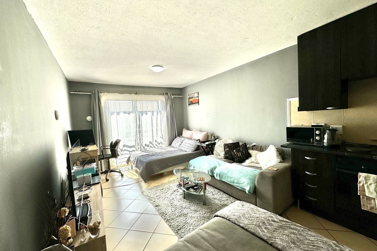 Open-plan living area featuring tiled flooring, a compact kitchen with dark cabinetry, and a sliding glass door providing access to the exterior.