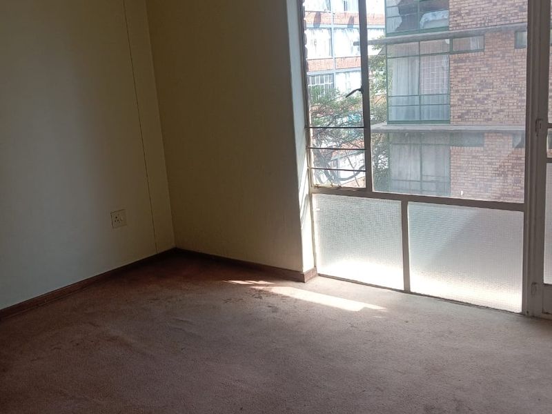 An empty bedroom featuring a large window with natural light and carpeted flooring, ready for renovation or staging.
