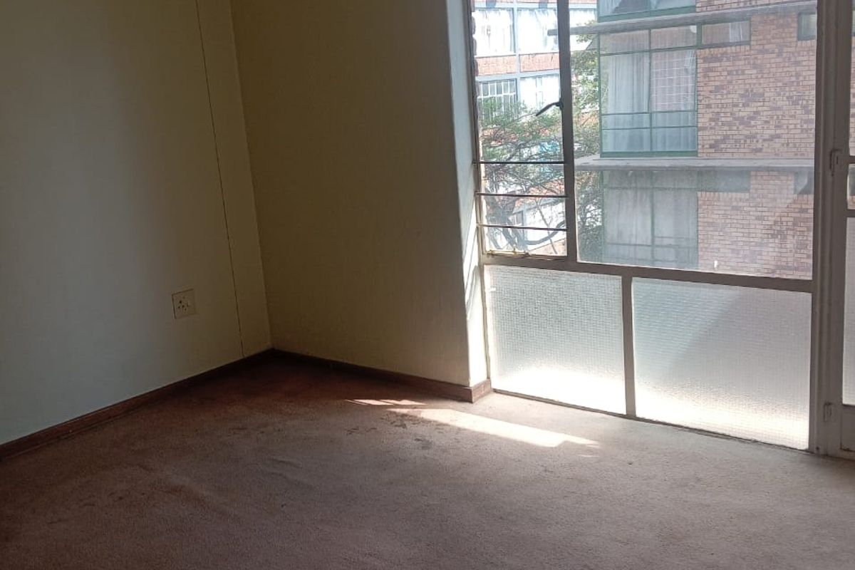 An empty bedroom featuring a large window with natural light and carpeted flooring, ready for renovation or staging.