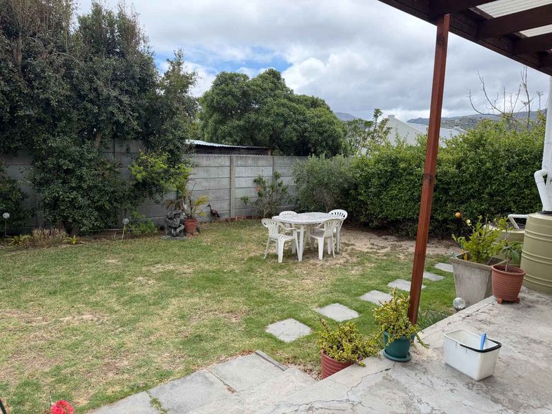 A private rear garden featuring a concrete patio area with a timber pergola, lawn, and perimeter boundary walling.