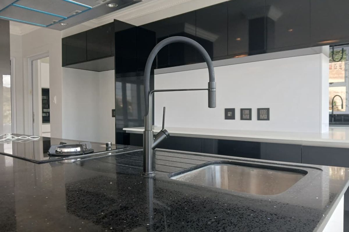 Modern kitchen featuring high-gloss black cabinetry, a central island with a built-in gas hob, and a sleek stainless steel sink with a contemporary faucet.
