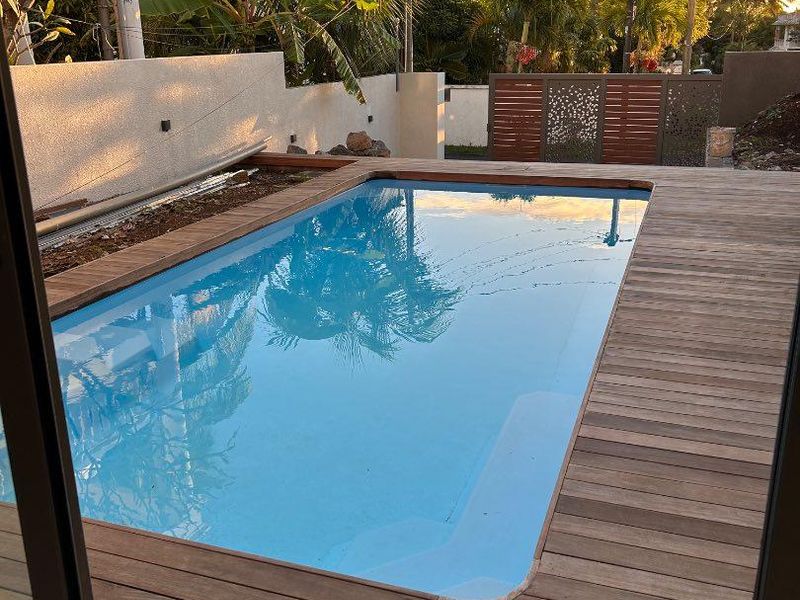 A well-maintained swimming pool area featuring timber decking, a boundary wall, and decorative privacy screening in a landscaped garden setting.