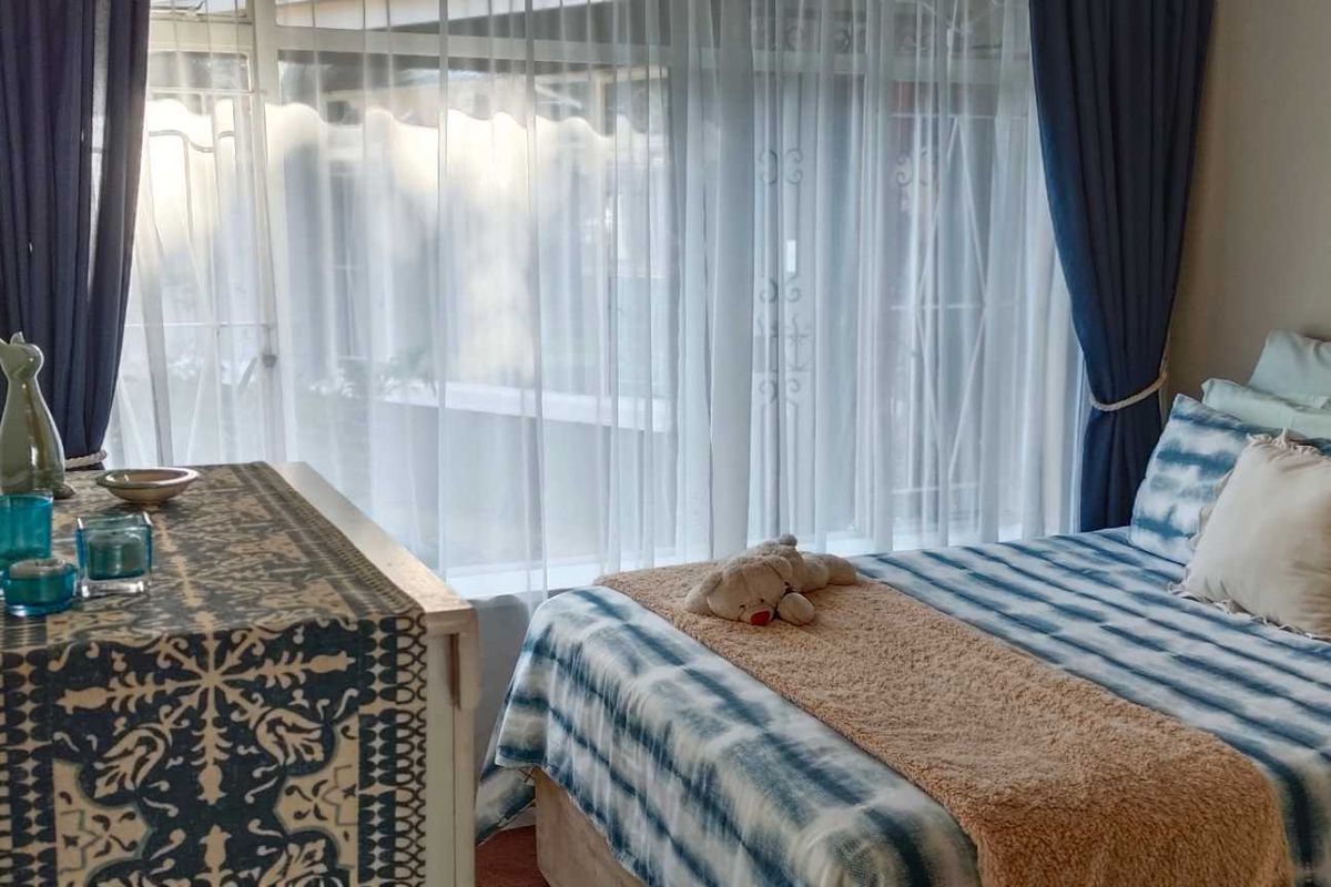 A cozy bedroom featuring large windows with sheer curtains, providing natural light and a view of the exterior.