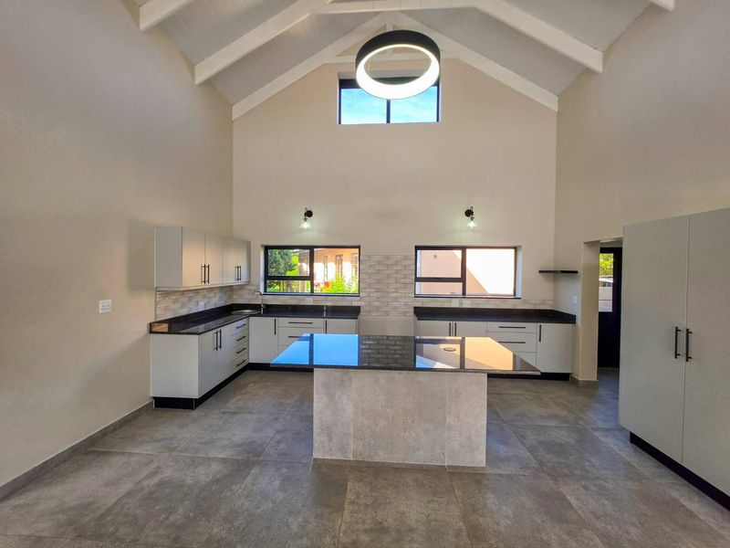 Modern, spacious kitchen featuring a central island, granite countertops, sleek cabinetry, and a high vaulted ceiling with contemporary lighting.