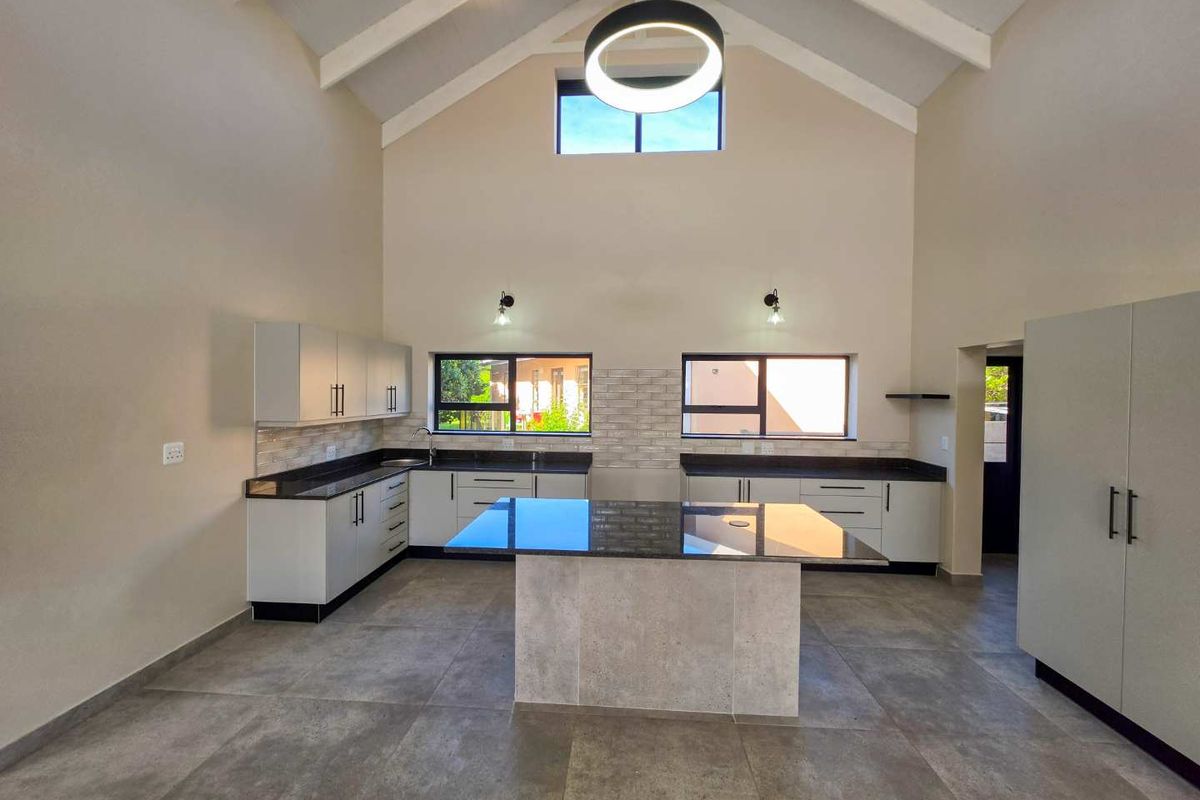 Modern, spacious kitchen featuring a central island, granite countertops, sleek cabinetry, and a high vaulted ceiling with contemporary lighting.