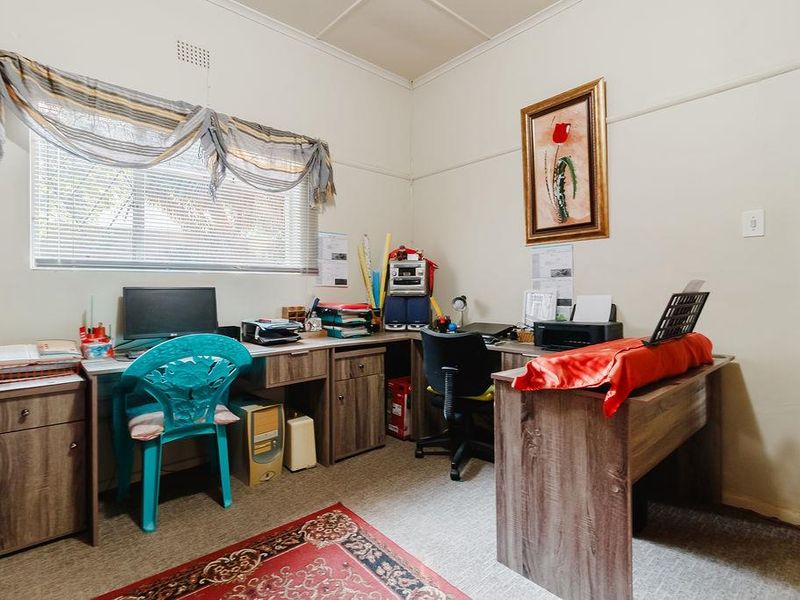A functional home office space featuring a window with natural light, neutral wall finishes, and a picture rail.