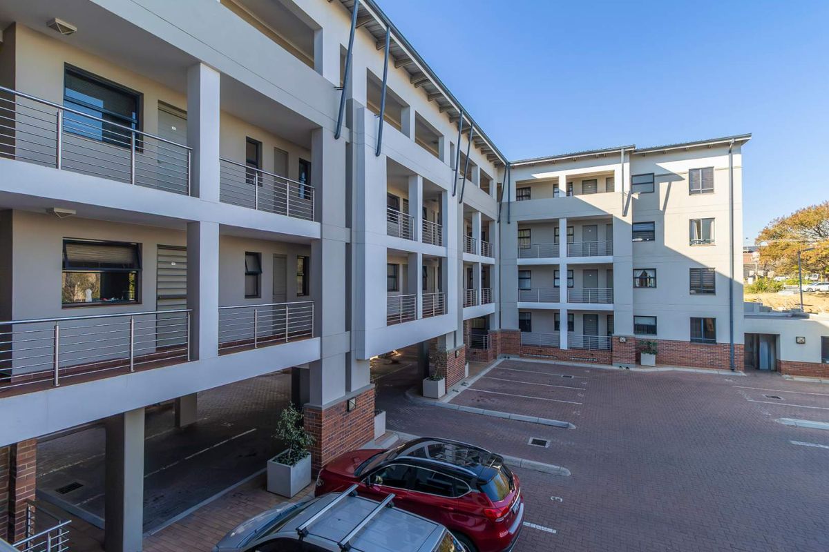 Exterior view of a modern multi-story apartment complex featuring paved parking bays and structured balcony access.