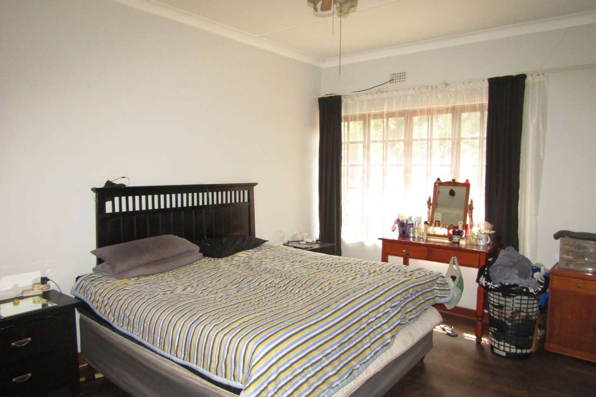 A standard bedroom featuring a large window, ceiling fan, and dark wood-look flooring.