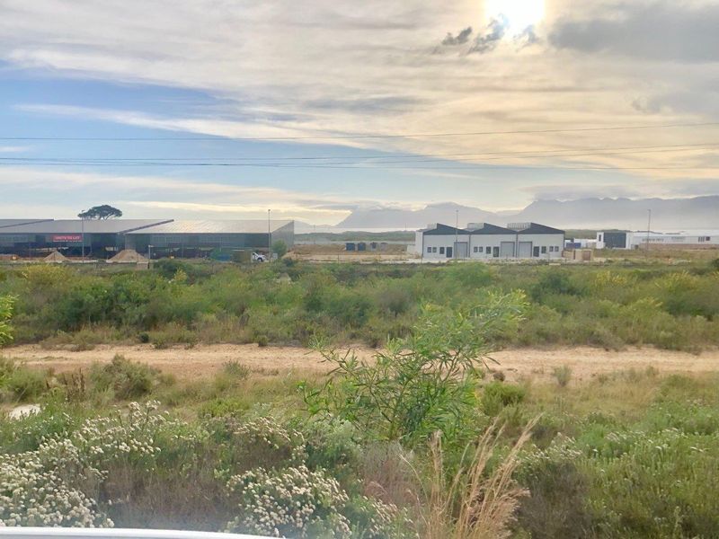 A wide-angle view of a commercial development site featuring warehouse units, natural vegetation, and distant mountain scenery.