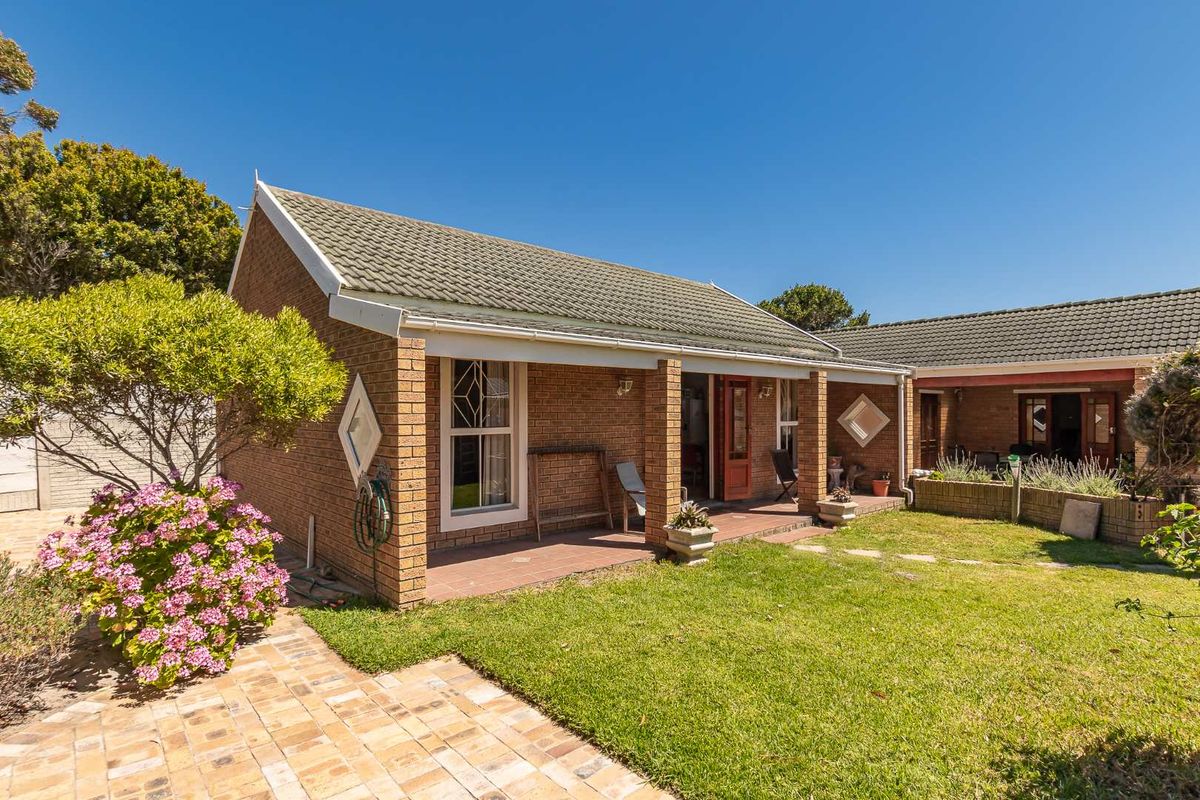 A view of the rear exterior of the house featuring a covered patio, brick facade, tiled roof, and a well-maintained garden area.