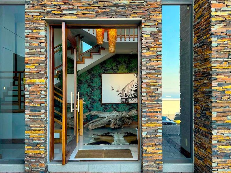 A striking entrance featuring a large timber pivot door framed by textured stacked stone cladding and full-height glass sidelights.