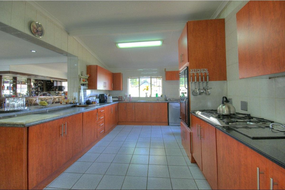 Spacious kitchen featuring wood-look laminate cabinetry, granite countertops, a gas hob, built-in oven, and tiled flooring with a breakfast bar pass-through.