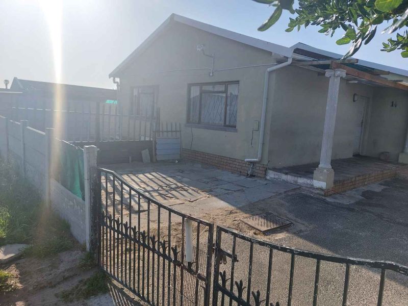 Front exterior view of a single-story house featuring a metal security gate, concrete driveway, and a covered porch area with a decorative column.