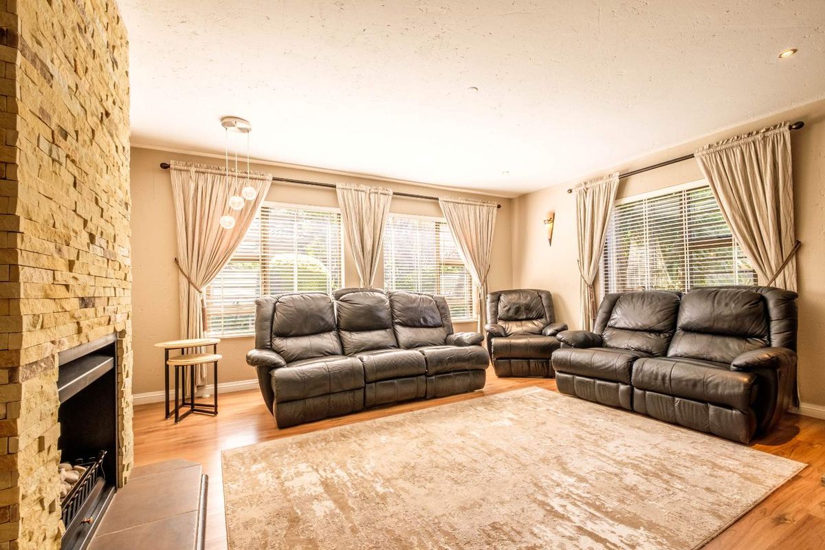 A spacious living room featuring a prominent stone-clad fireplace, laminate flooring, and large windows with venetian blinds, creating a warm and inviting atmosphere.
