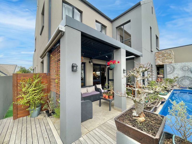 A modern covered patio area featuring timber decking, a pergola, and direct access to a swimming pool with a decorative stone feature wall.