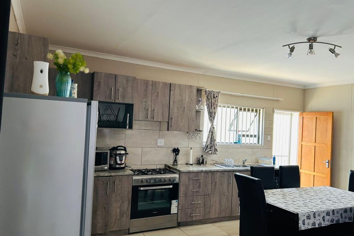Open-plan kitchen and dining area featuring modern wood-look cabinetry, gas hob, oven, tiled backsplash, and functional workspace with security bars on windows.