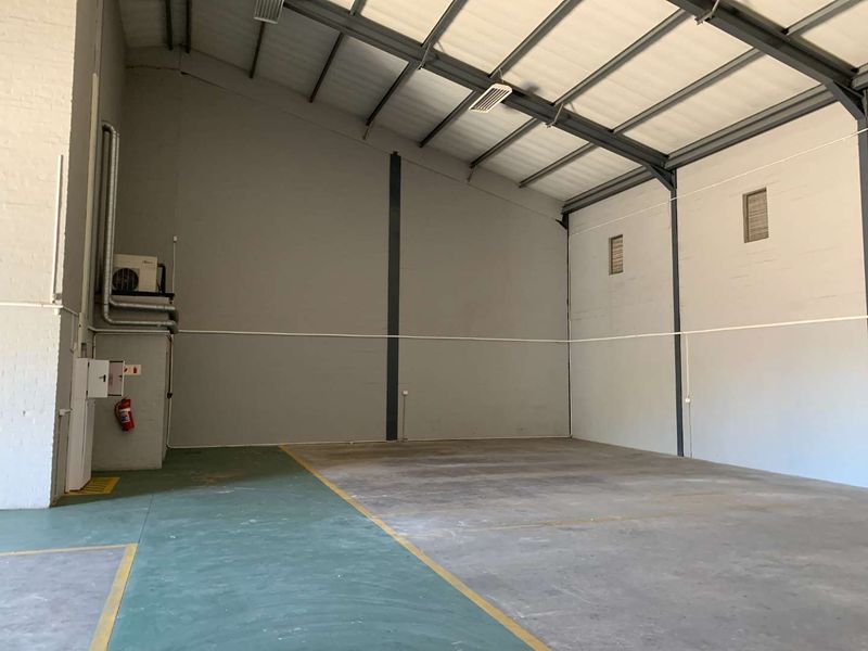 Spacious industrial utility area featuring high ceilings with exposed steel trusses, painted brick walls, and durable concrete flooring with marked floor zones.