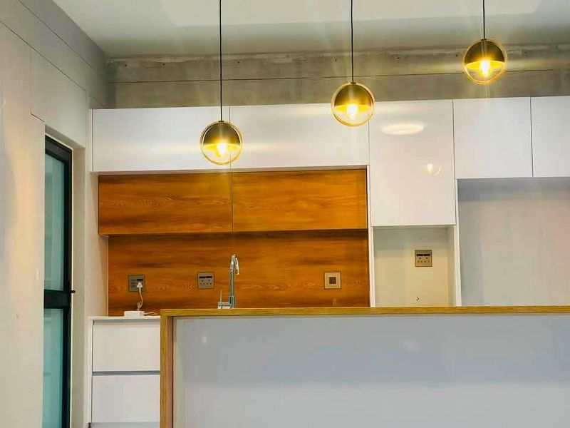 Modern kitchen featuring a central island, sleek white and wood-grain cabinetry, contemporary pendant lighting, and polished white tiled flooring.