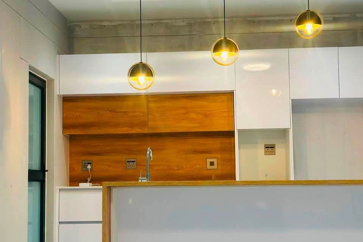 Modern kitchen featuring a central island, sleek white and wood-grain cabinetry, contemporary pendant lighting, and polished white tiled flooring.