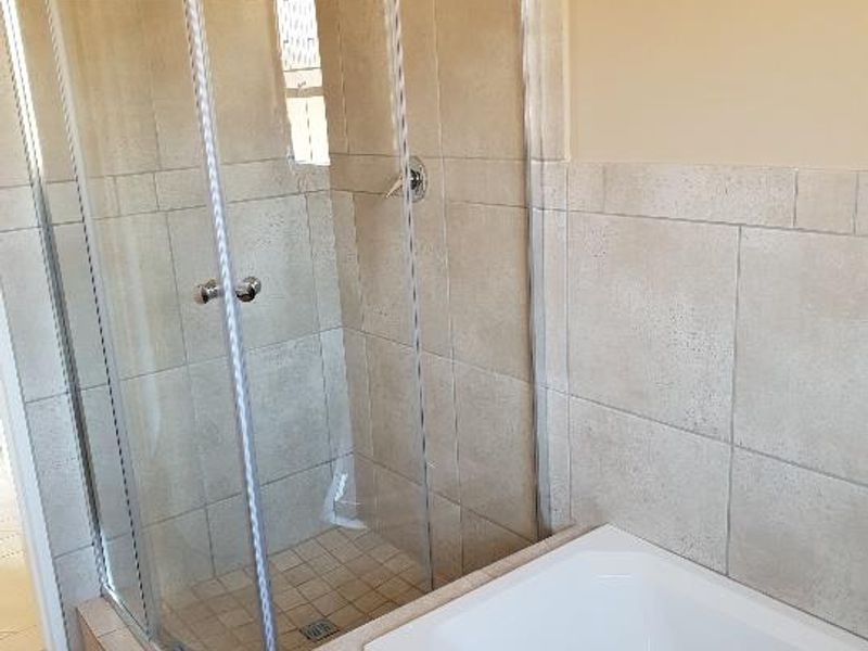 A functional bathroom featuring a corner shower enclosure and a built-in bathtub with neutral ceramic tiling throughout.