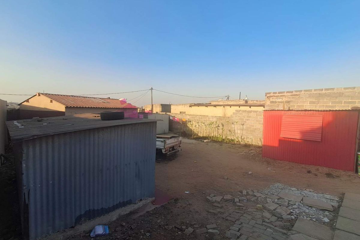 Rear yard area featuring corrugated metal structures, concrete block boundary walls, and a partially paved ground surface.