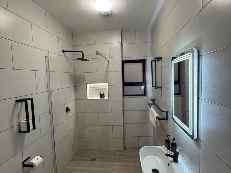 Modern bathroom featuring a walk-in shower with a recessed niche, wall-mounted basin, and a contemporary LED vanity mirror with sleek black matte fixtures.