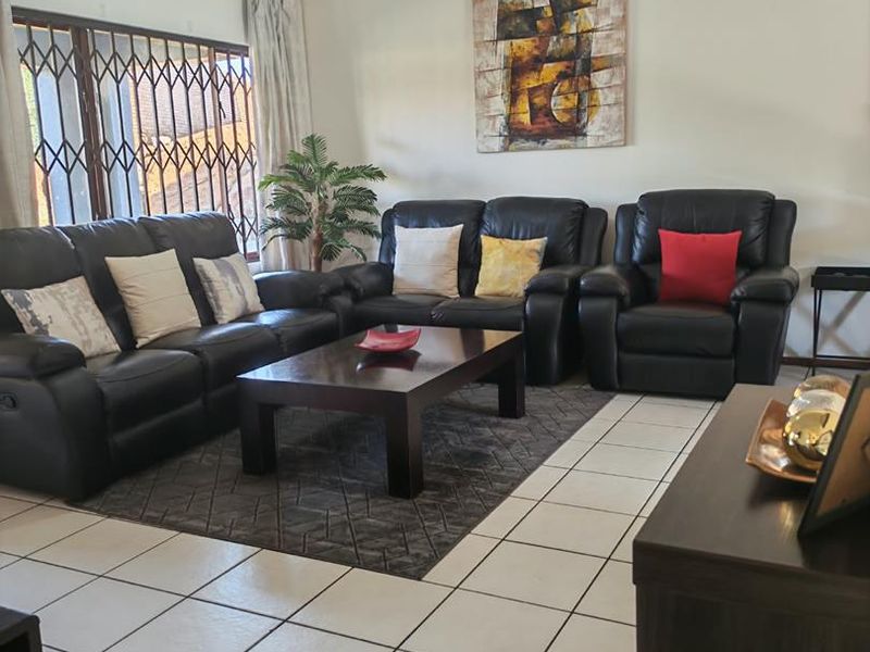 A comfortable living room featuring ceramic floor tiles and a large window with a fitted security gate.