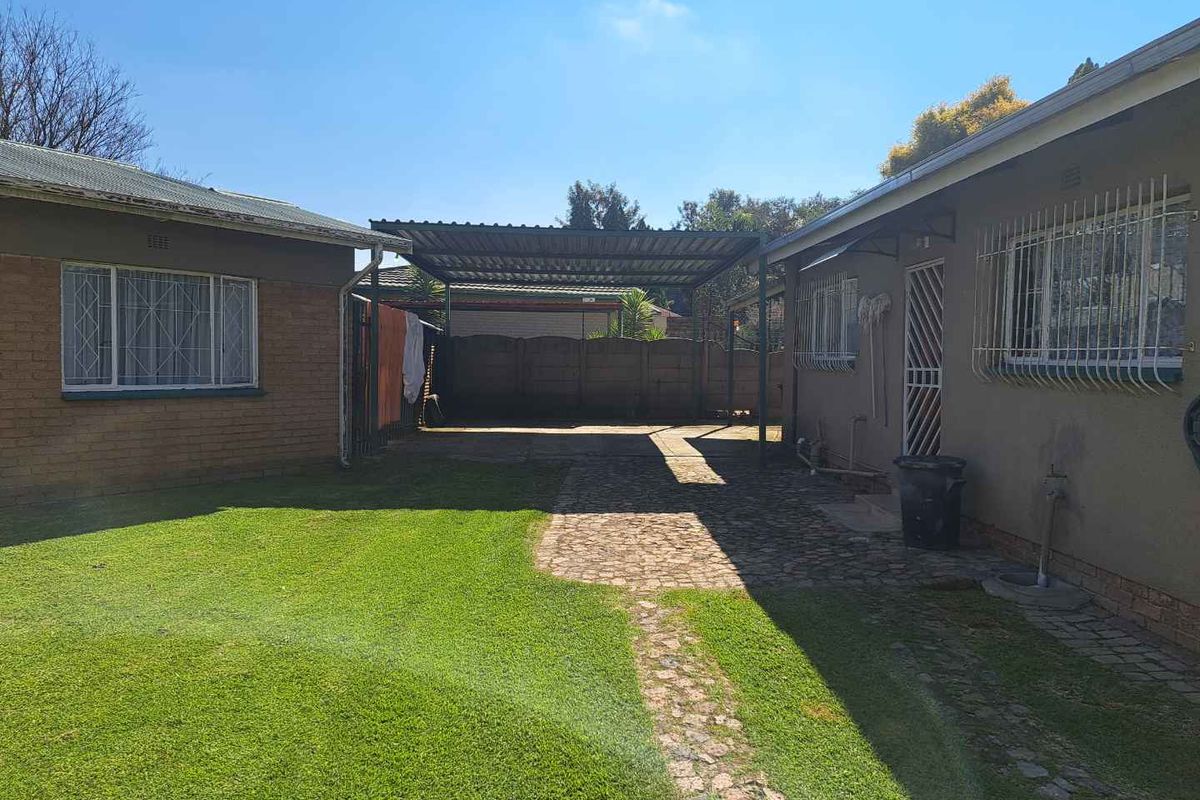 Rear exterior view featuring a paved driveway, covered carport, and a well-maintained lawn area between two residential building sections.